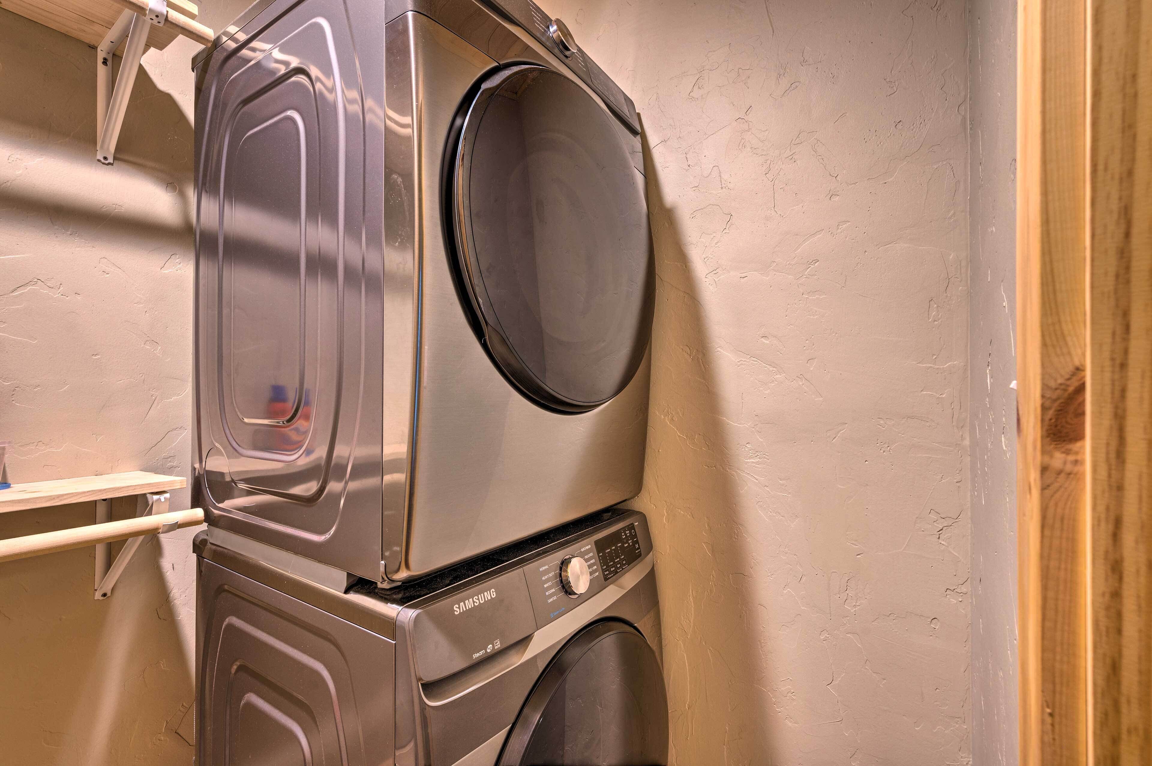 Un appareil combiné lave-linge et sèche-linge, de type « superposé », doté d’un panneau de commande et d’une étagère en bois.