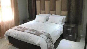 A bedroom with a large bed, a headboard, a nightstand, and a dresser. - Caribbean Estates Villa & Apt (Port Edward)