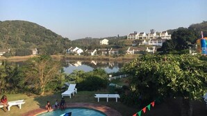 A residential area with a swimming pool surrounded by greenery, a lake in the background, and houses with white exteriors. - Caribbean Estates Villa & Apt (Port Edward)