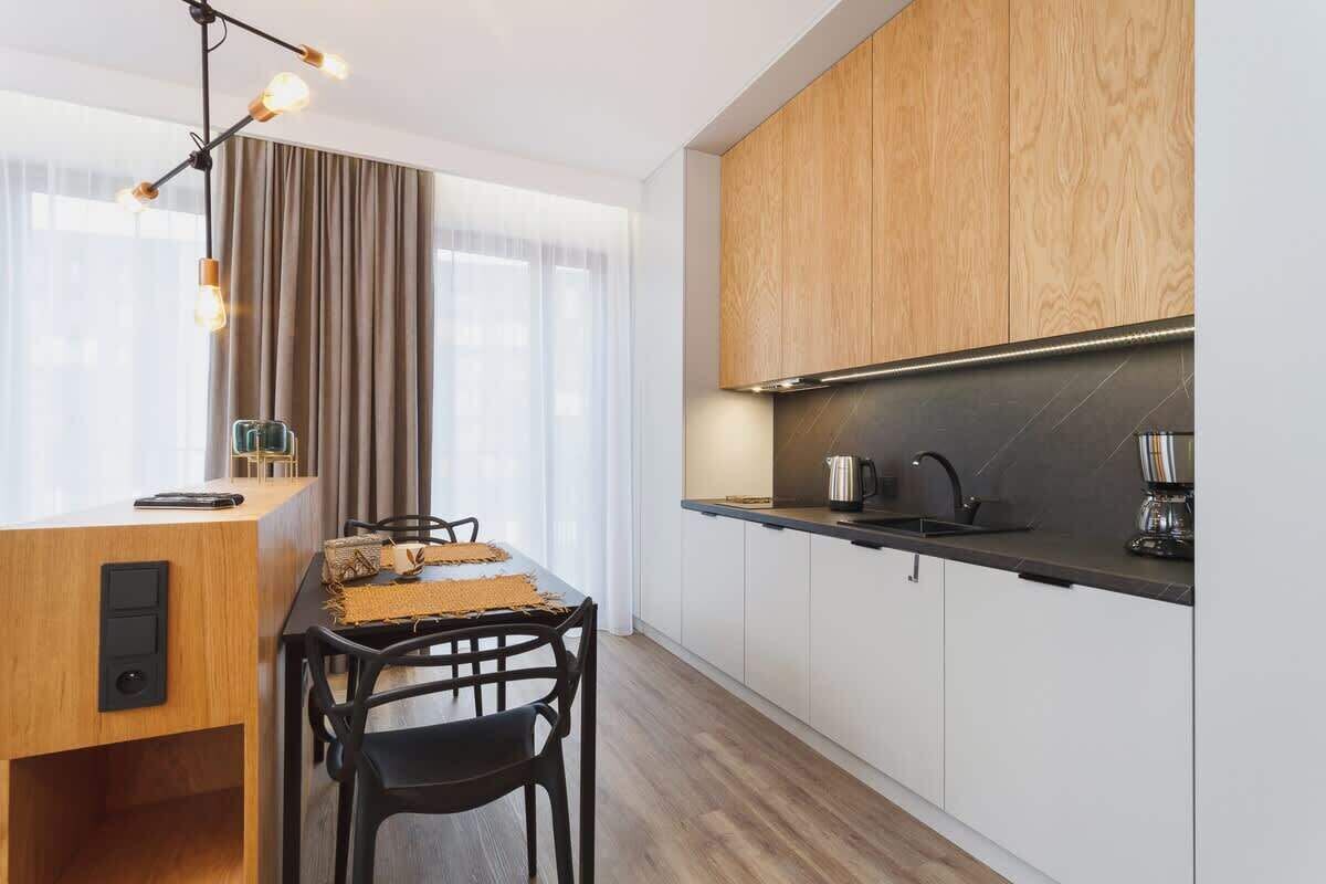 A modern kitchen with wooden cabinets, a black countertop, and a dining area with a table and chairs.