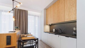 A modern kitchen with wooden cabinets, a black countertop, and a dining area with a table and chairs. - Cracow | Rakowicka 22J | Intimate Studio | Air Conditioning (Kraków)