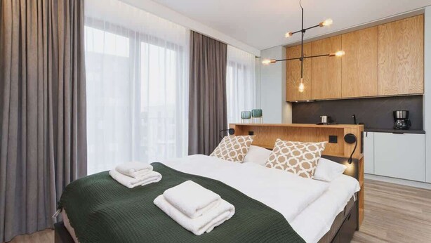 A modern hotel room with a large bed, a kitchenette, and a view of the city. - Cracow | Rakowicka 22J | Intimate Studio | Air Conditioning (Kraków)