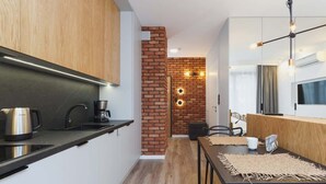 A modern kitchen with a brick accent wall, a dining area with a table and chairs, and a TV mounted on the wall. - Cracow | Rakowicka 22J | Intimate Studio | Air Conditioning (Kraków)