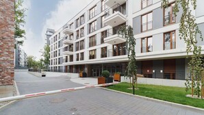 A modern multi-story residential building with balconies, a paved courtyard, and a brick wall on the left. - Cracow | Rakowicka 22J | Intimate Studio | Air Conditioning (Kraków)