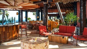 Un espace de détente extérieur aménagé avec des meubles en bois, un foyer en pierre et une vue sur l’océan.