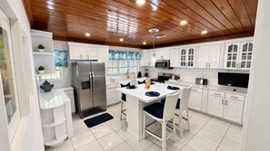 A modern kitchen with white cabinetry, a stainless steel refrigerator, a microwave, and a dining area with a white table and blue chairs.
