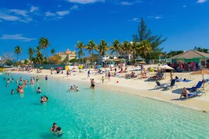 Una spiaggia con acque turchesi cristalline, palme e bagnanti.