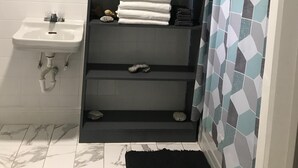 Een badkamer met een wit wastafelmeubel, een spiegel, een handdoekhouder, planken met opgevouwen handdoeken en een douchegordijn met een geometrisch patroon.