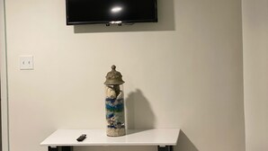 Een kamer met een wandgemonteerde flatscreen-tv, een klein wit tafeltje met een decoratieve glazen vaas, en een afstandsbediening op het tafeltje.