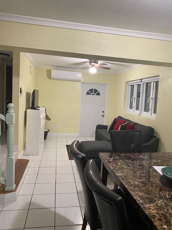 A dining area with a marble table and chairs, a white refrigerator, a grey sofa, and a ceiling fan.
