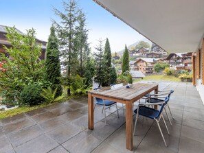 A wooden table with chairs on a patio with a view of houses and trees. - Fortuna Apt.M by Interhome (Wengen)