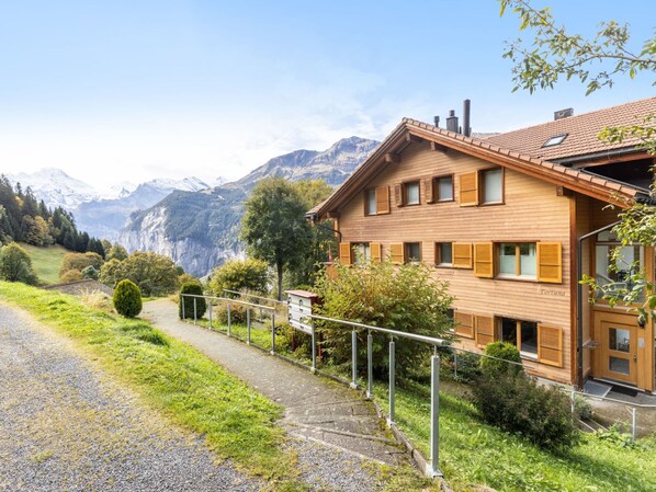 A wooden house with a balcony, surrounded by greenery and mountains in the background. - Fortuna Apt.M by Interhome (Wengen)