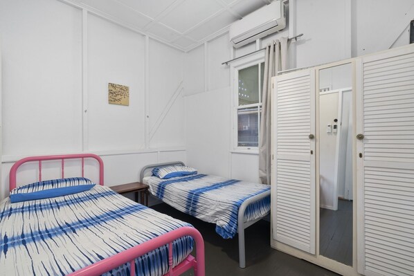 A dormitory room with two beds, a window, an air conditioning unit, and a wardrobe.