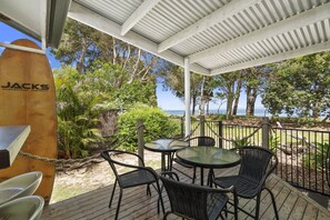 An outdoor patio with a covered seating area, a surfboard, and a view of the ocean.