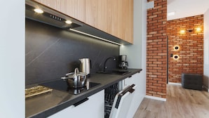 A modern kitchen with a black countertop, stainless steel appliances, and a brick accent wall. - Wooden Studio with Balcony | Parking | Close to Station (Kraków)