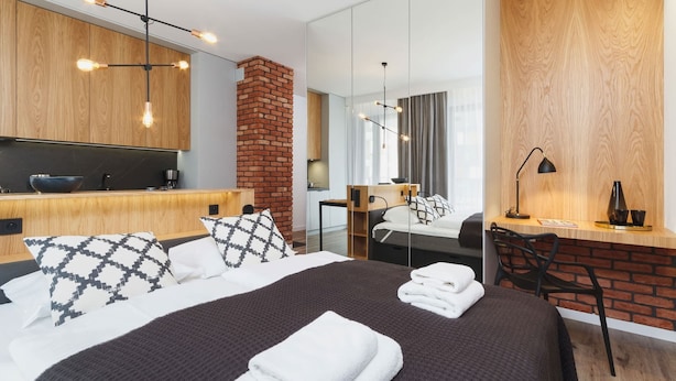 A modern hotel room with a large bed, a desk, a brick accent wall, and a large mirror. - Wooden Studio with Balcony | Parking | Close to Station (Kraków)