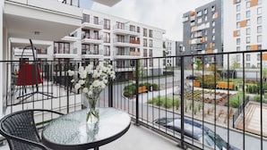 A balcony with a glass table and chairs, a vase of flowers, and a view of modern apartment buildings. - Wooden Studio with Balcony | Parking | Close to Station (Kraków)