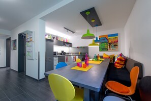 Una cocina moderna con comedor, que presenta una mesa larga, sillas coloridas y lámparas colgantes.