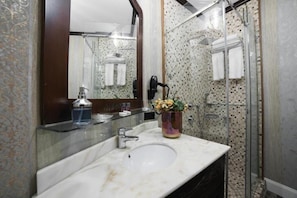 A bathroom with a marble sink, a glass shower enclosure, and a mirror with a decorative frame. - Medar Hotel (Istanbul)