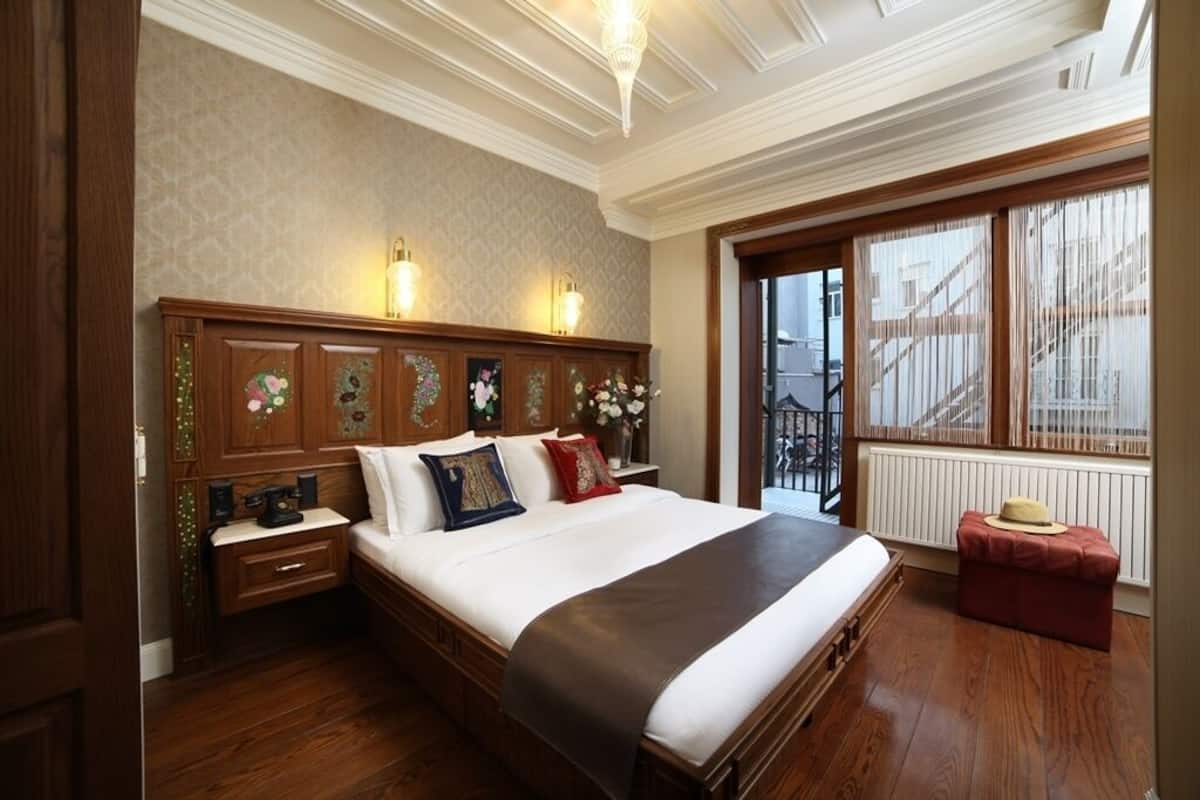A bedroom with a large bed, wooden headboard, bedside lamps, a nightstand, and a window with a view of the outside.