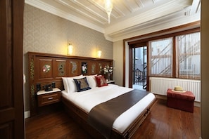 A bedroom with a large bed, wooden headboard, bedside lamps, a nightstand, and a window with a view of the outside. - Medar Hotel (Istanbul)
