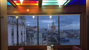 A restaurant with a view of a cityscape, featuring a table and two red cushioned booths. - Medar Hotel (Istanbul)