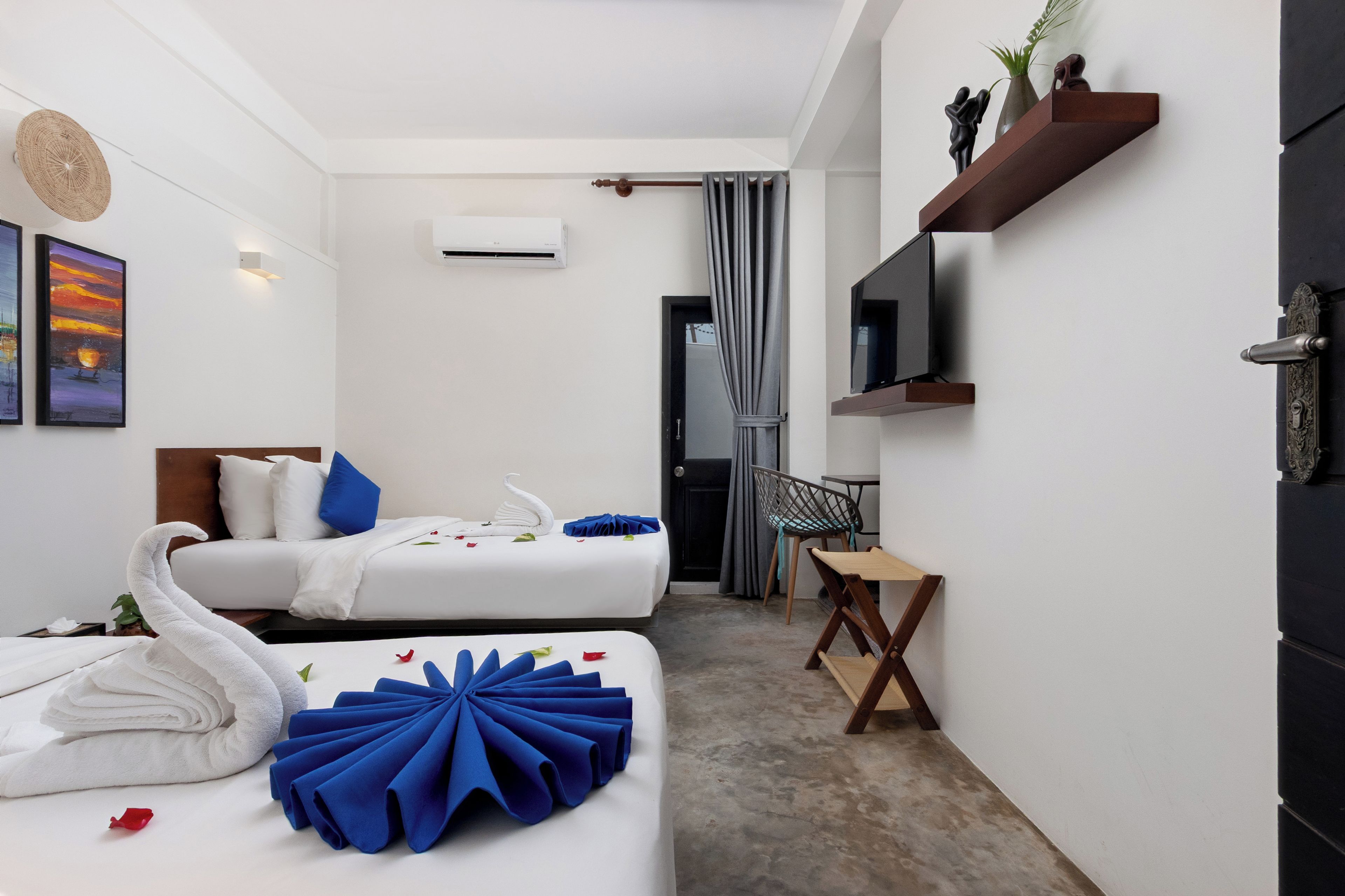 A hotel room with two beds, a desk, a TV, and a shower area.