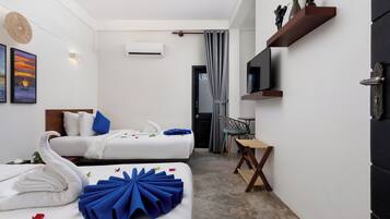 A hotel room with two beds, a desk, a TV, and a shower area.