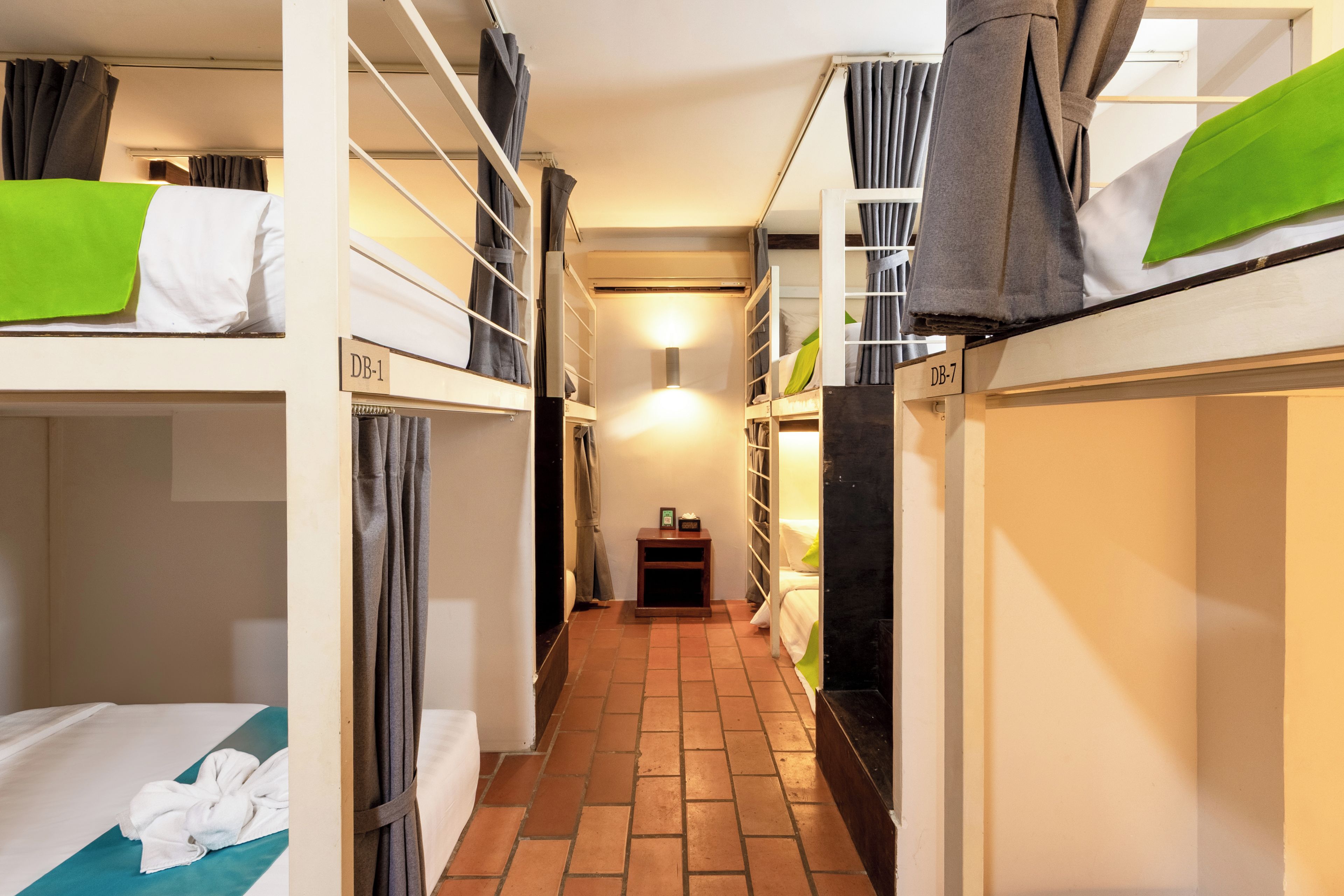 A narrow corridor with bunk beds, each labeled with a number, and a small table with a lamp in the center.