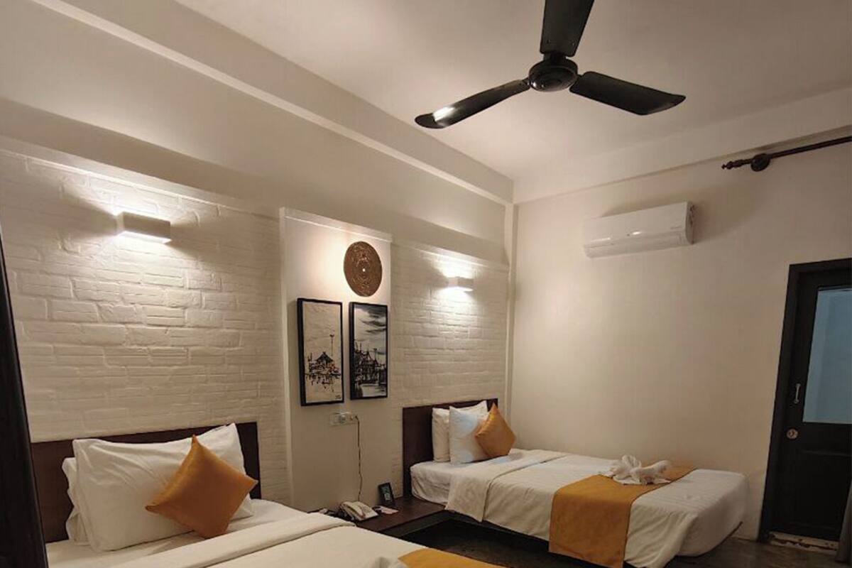 A hotel room with two beds, a ceiling fan, a brick wall, and a door.