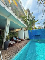 Uma área à beira da piscina com espreguiçadeiras, um deck de madeira e uma piscina com azulejos azuis.