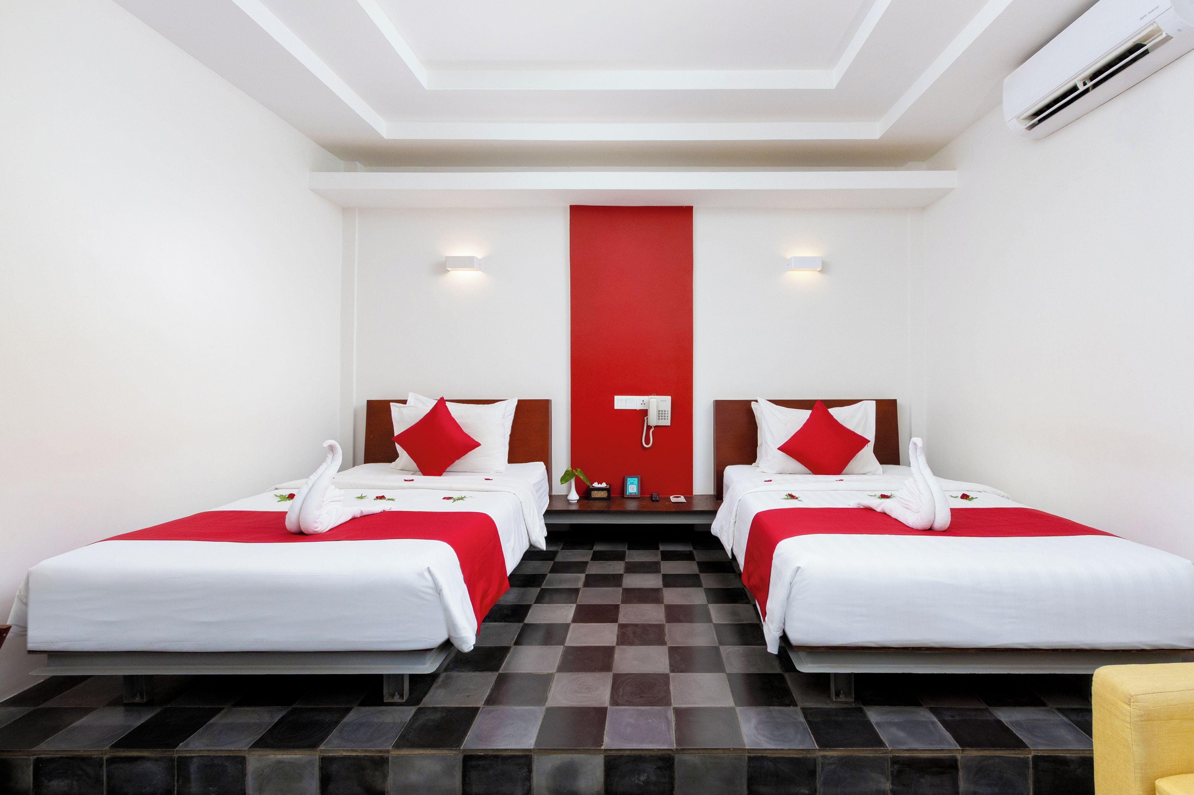 A hotel room with two beds, a red accent wall, checkered floor tiles, and a small yellow chair.