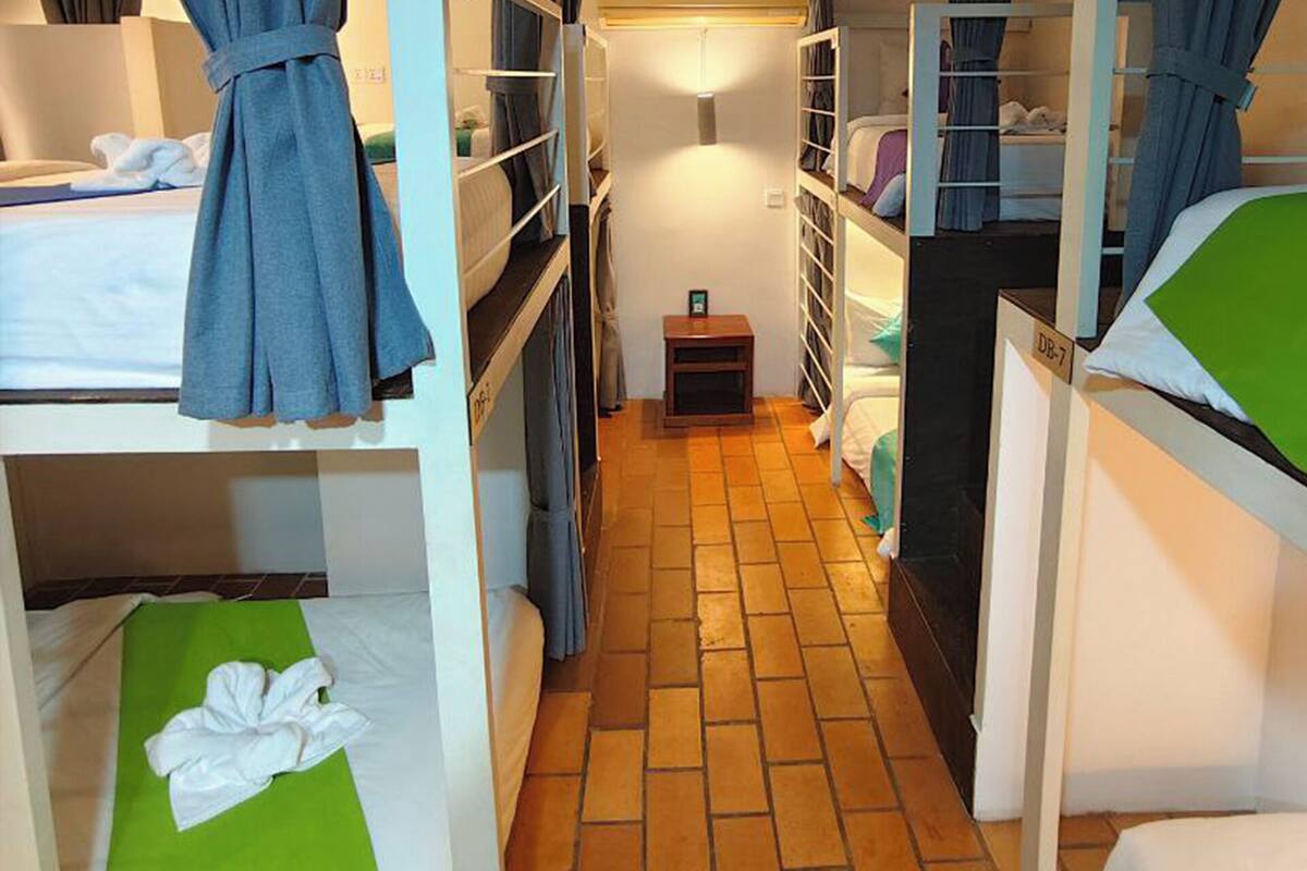 A narrow corridor with bunk beds on either side, a small table with a lamp, and a tiled floor.