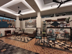 A modern interior with a checkered floor, a sofa, a dining table with chairs, ceiling fans, and a wall with a cityscape painting. - Baahu Villa (Siem Reap)