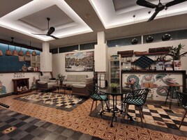 Um interior moderno com piso xadrez, um sofá, uma mesa de jantar com cadeiras, ventiladores de teto e uma parede com uma pintura de paisagem urbana.