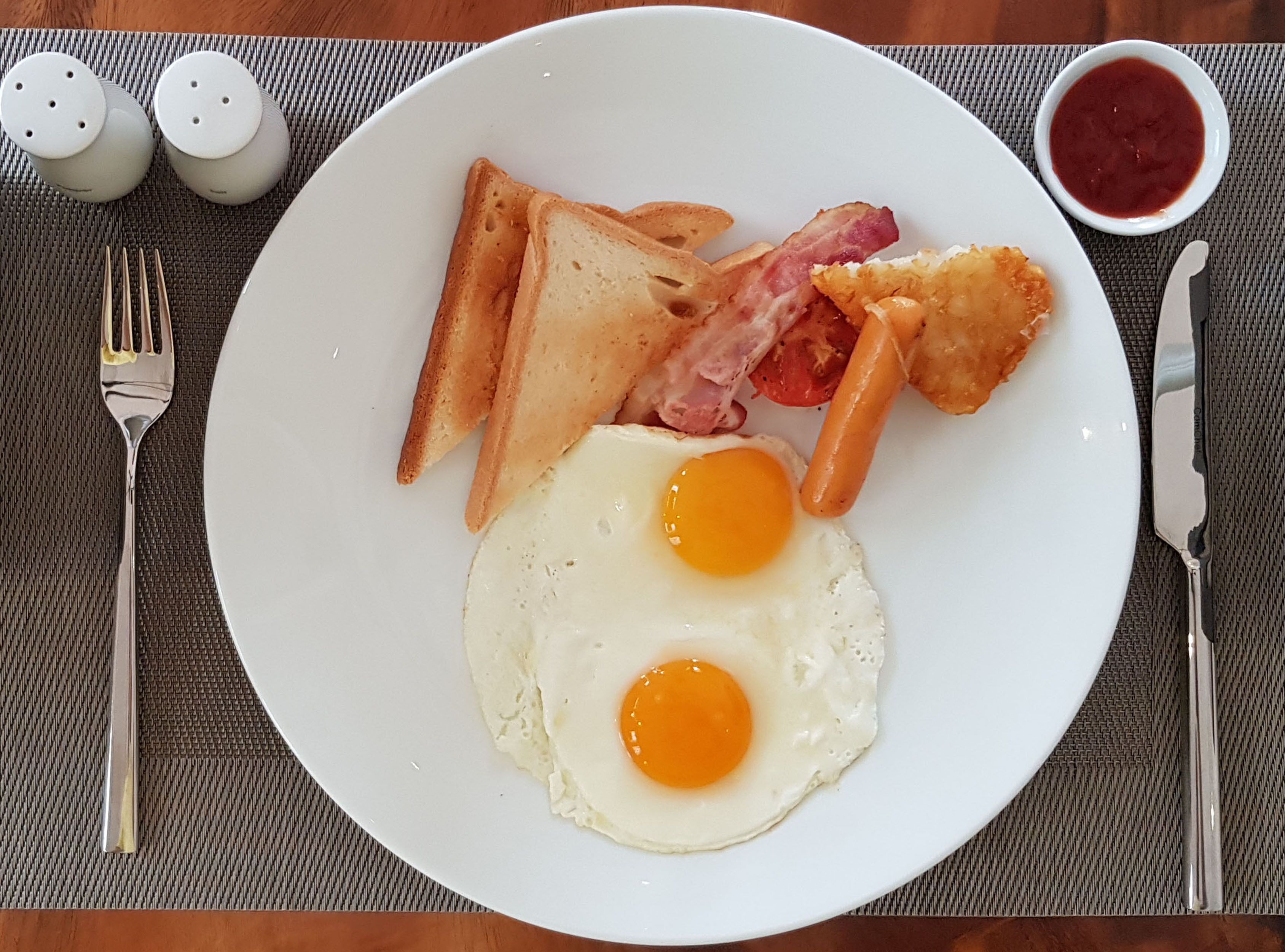Un plato de desayuno con huevos, tocino, tostadas y patatas ralladas sobre un plato blanco.