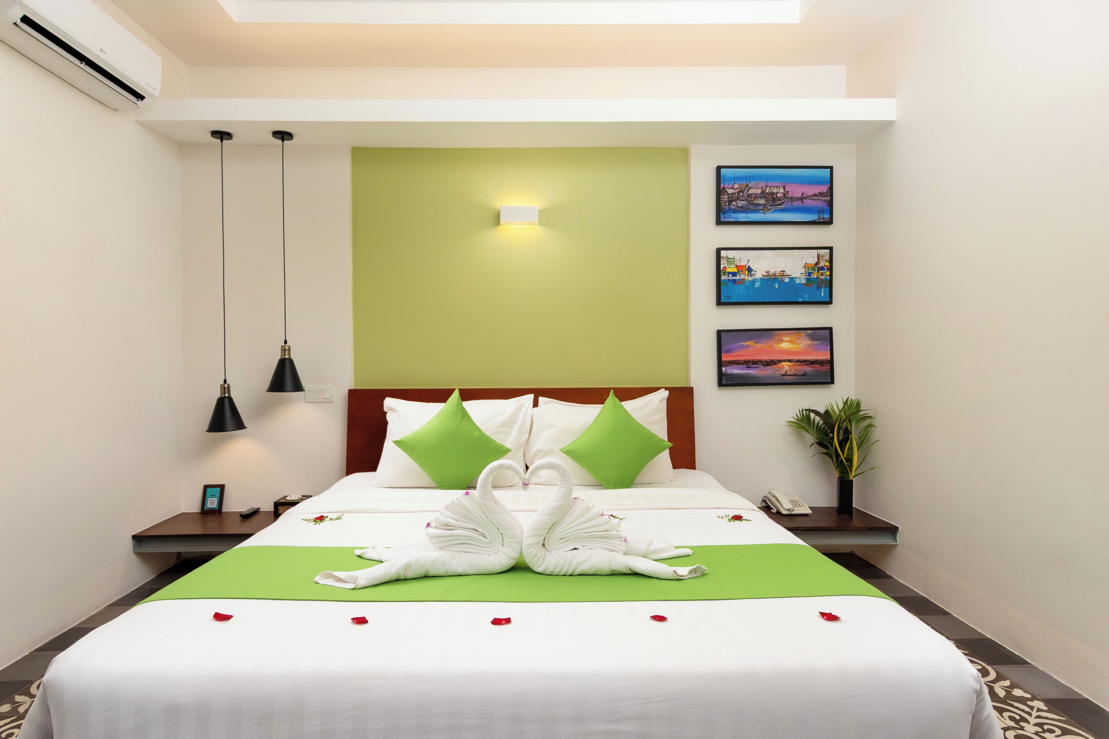 Une chambre d’hôtel avec un lit bien fait, un mur vert et trois tableaux encadrés.