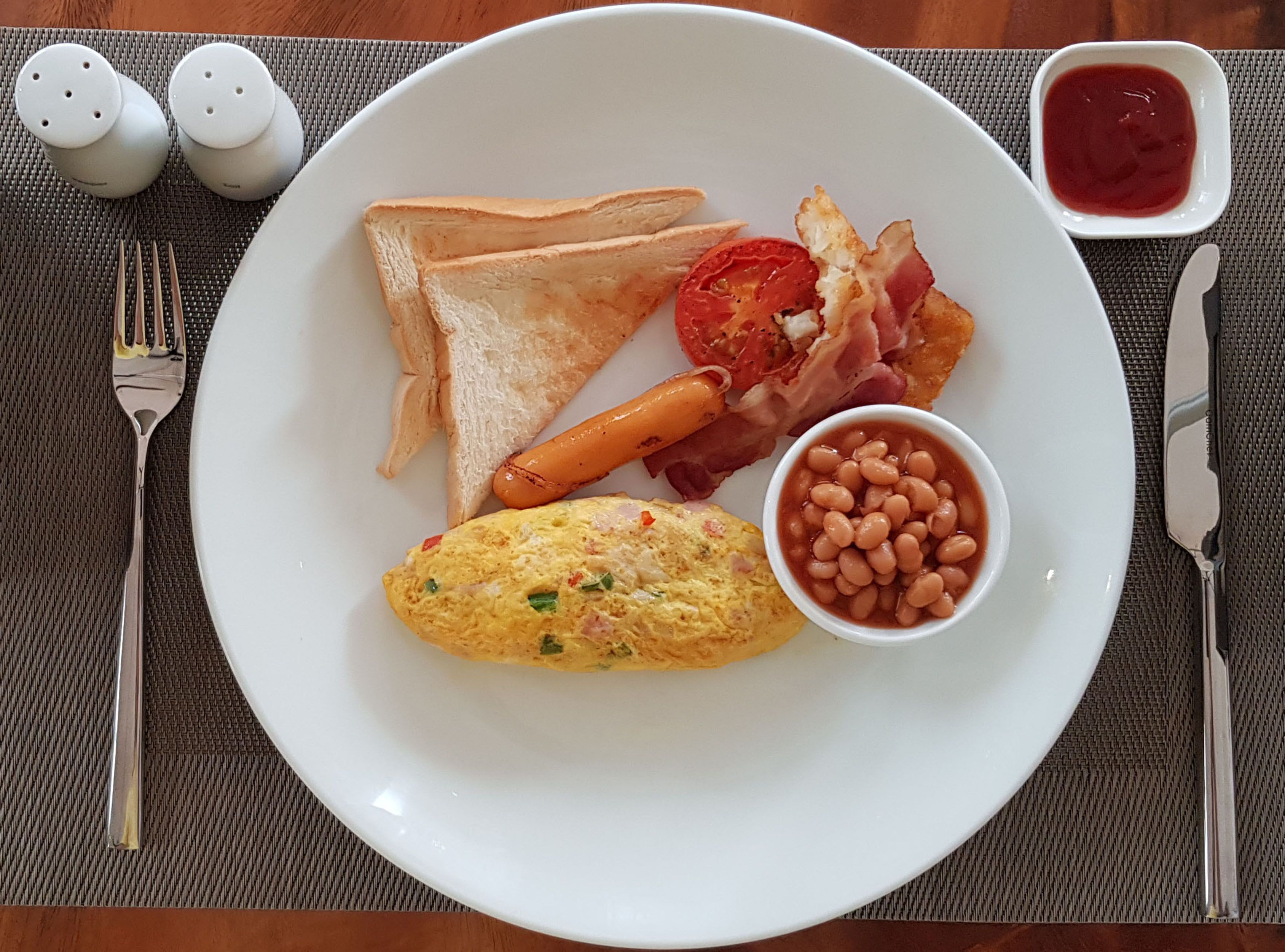 Un plato con tostadas, tocino, tomate, frijoles y un huevo.