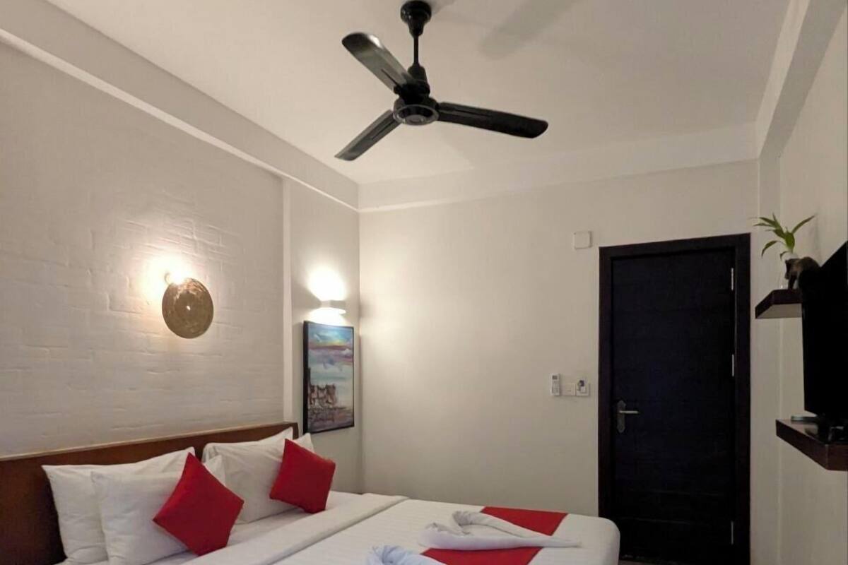 A hotel room with a bed, a ceiling fan, a door, and a wall-mounted light fixture.