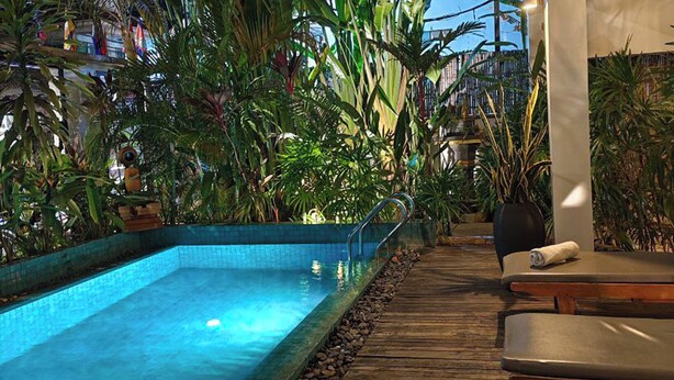 A pool area with a wooden deck, surrounded by lush tropical plants. - Baahu Villa (Siem Reap)
