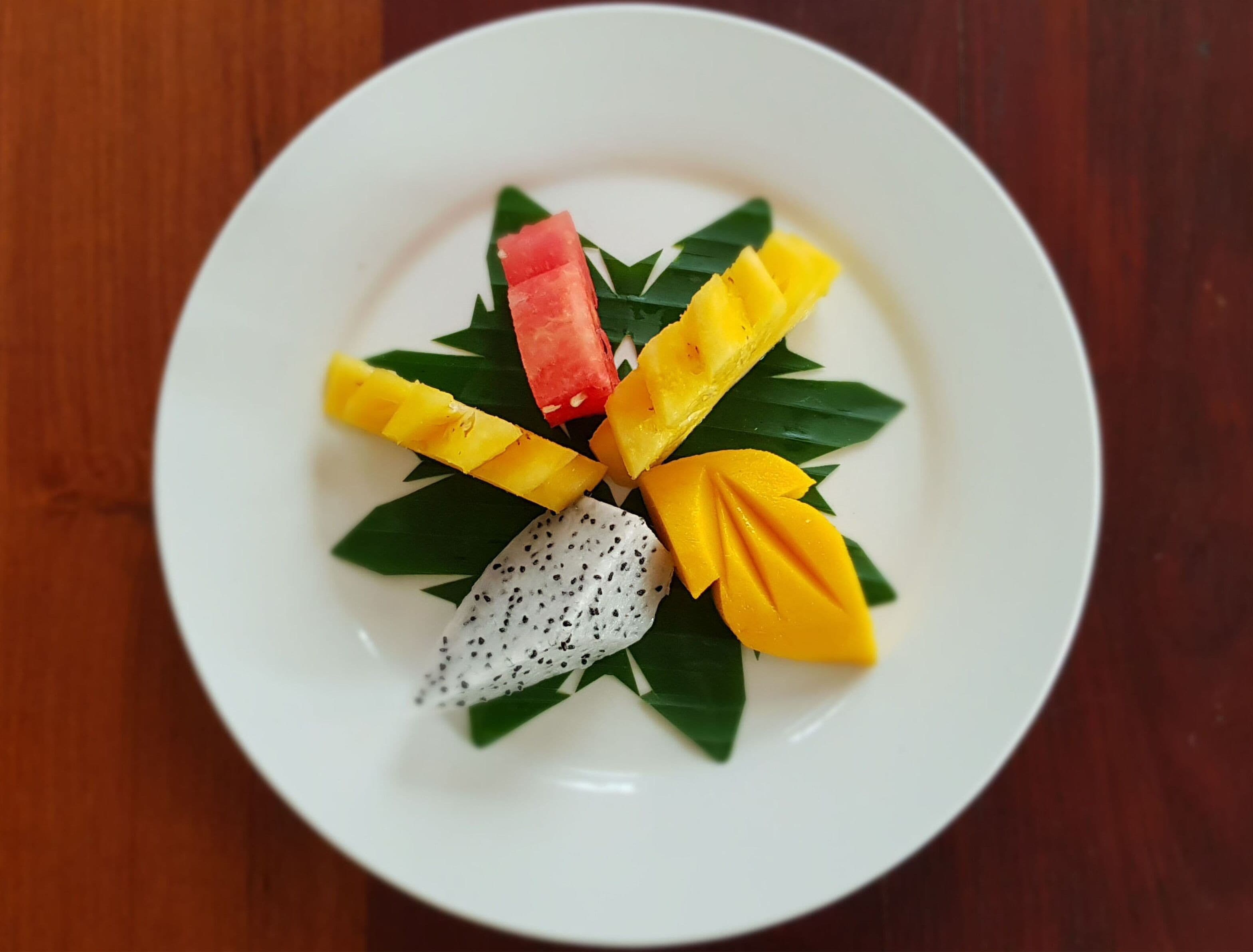 Un plato blanco con una composición de frutas sobre una mesa de madera.