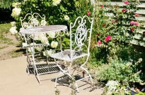 Ein Tisch- und Stuhlgarnitur aus Metall in einem Garten mit üppigem Grün und Blumen.