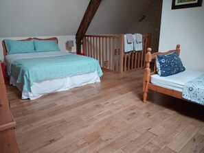 Un dormitorio con dos camas, piso de madera, una escalera y una lámpara fijada a la pared.