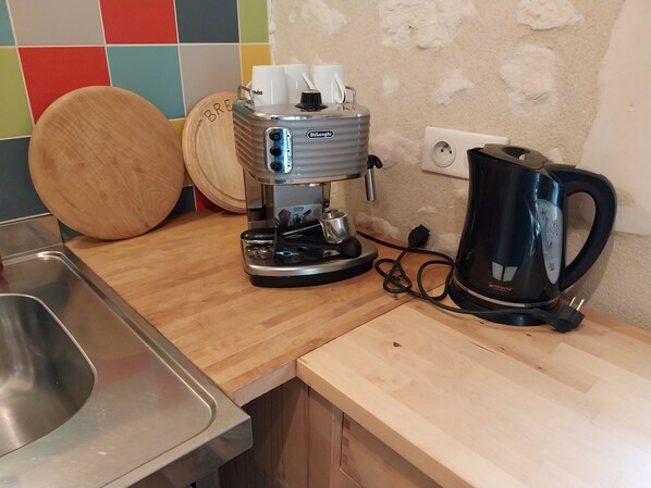 A kitchen with a coffee maker, a kettle, and a wooden cutting board.