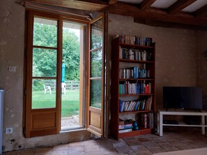 Une pièce avec une bibliothèque en bois, un téléviseur posé sur un meuble et une porte-fenêtre coulissante donnant sur un jardin.
