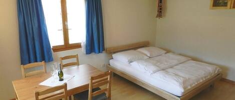 Una habitación con una cama de madera, una mesa de madera con dos sillas y una ventana con cortinas azules.