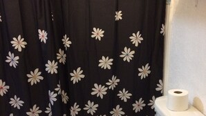 Une salle de bain avec des toilettes, un rouleau de papier toilette posé sur le réservoir, et un rideau de douche orné d’un motif floral.