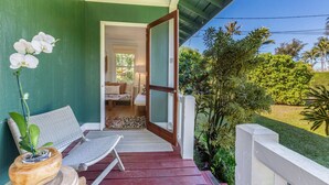 Un porche con un banco de madera, una orquídea en maceta y vistas a un dormitorio con cama y ventana.