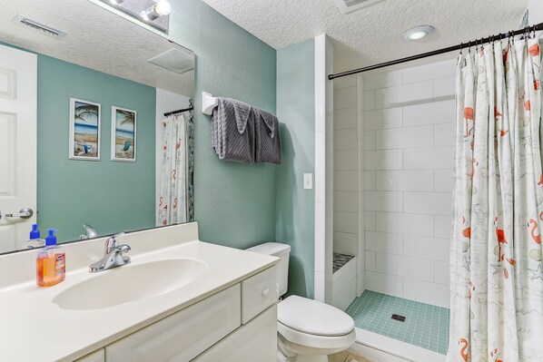 Un baño con lavamanos blanco, inodoro y ducha con cortina estampada.