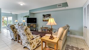 Ein Wohnzimmer mit einer Couch, Sesseln, einem Couchtisch, einem Fernseher und einem Bücherregal.